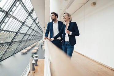 Lächelnde männliche und weibliche Unternehmer stehen an einem Geländer im Büro - JOSEF04861