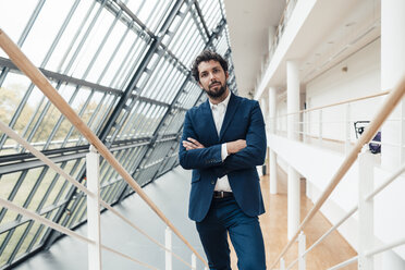 Confident businessman with arms crossed standing in office - JOSEF04864