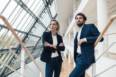 Male and female professionals looking away while standing in office - JOSEF04865