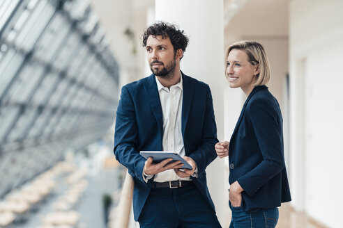 Business partners with digital tablet looking away while standing at office - JOSEF04868