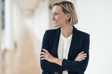 Smiling businesswoman with arms crossed looking away in office - JOSEF04872