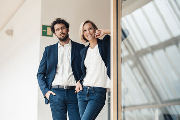 Smiling businesswoman looking away while standing with colleague at office - JOSEF04876