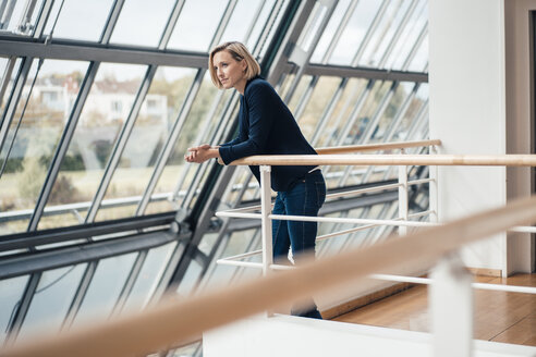 Weibliche Unternehmerin schaut weg, während sie sich auf ein Geländer stützt - JOSEF04878