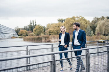 Männliche und weibliche Unternehmer lächelnd beim Gehen auf einer Brücke - JOSEF04881
