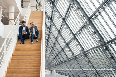 Male and female colleagues using digital tablet while sitting on steps - JOSEF04885