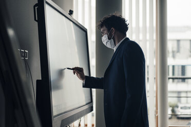 Männlicher Unternehmer mit Gesichtsmaske, der auf einer Projektionsfläche im Büro schreibt - JOSEF04890