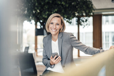 Unternehmerin mit Mobiltelefon lächelnd im Büro - JOSEF04904