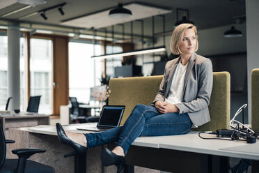 Female entrepreneur looking away while sitting on desk in office - JOSEF04905