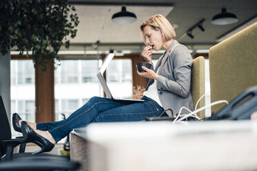 Unternehmerin beim Essen, während sie im Büro einen Laptop benutzt - JOSEF04906