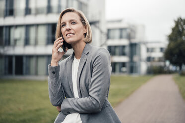 Female entrepreneur talking on mobile phone while standing at office park - JOSEF04914