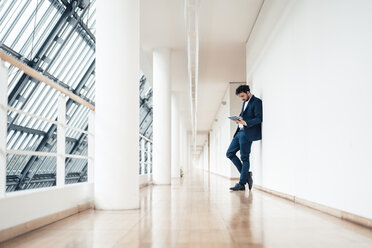 Male entrepreneur using digital tablet while standing at office corridor - JOSEF04921