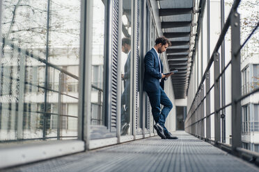 Male entrepreneur using digital tablet while standing at corridor - JOSEF04926