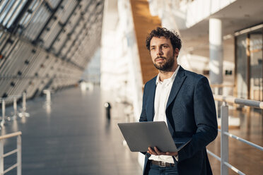 Männlicher Unternehmer mit Laptop, der wegschaut, während er in der Büro-Lobby steht - JOSEF04929