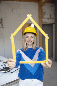 Smiling female architect looking through house shaped folded ruler at site - HMEF01300