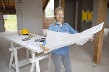 Lächelnde Designerin bei der Arbeit mit einem Bauplan auf der Baustelle - HMEF01312
