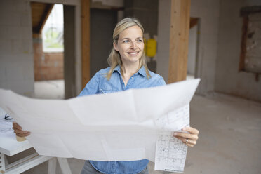 Lächelnde Architektin, die den Blick abwendet, während sie einen Bauplan auf der Baustelle hält - HMEF01313