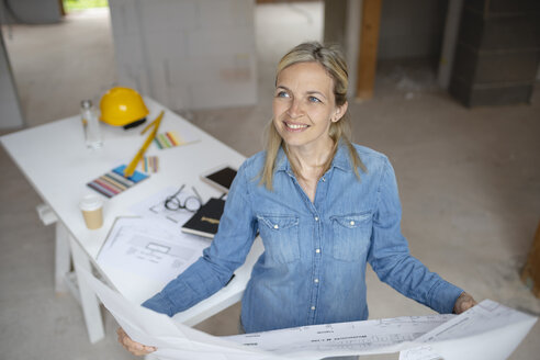 Female building contractor looking away holding blueprint at site - HMEF01314
