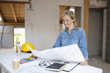 Lächelnde Architektin mit Bauplanung am Tisch in einer Wohnung - HMEF01315