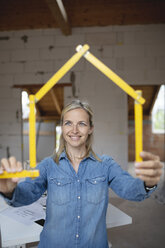 Lächelnde Architektin, die auf einer Baustelle mit einem Zollstock ein Haus formt - HMEF01316
