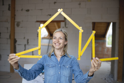 Happy female architect making house shape with folding ruler at site - HMEF01317