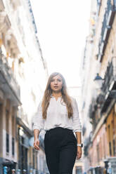 Beautiful young woman looking away while walking at alley - DAMF00823