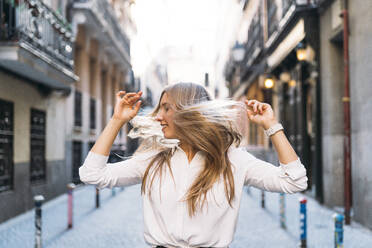 Young blond woman tossing hair while standing at alley - DAMF00830