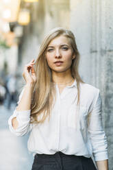 Junge Frau mit blondem Haar an der Wand stehend - DAMF00836