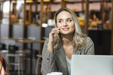 Beautiful female professional talking on smart phone while sitting in cafe - PNAF01971