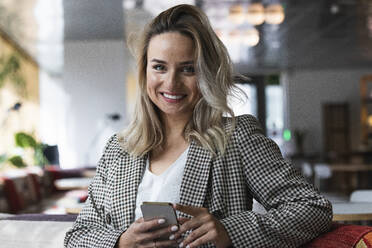 Beautiful female professional holding mobile phone at cafe - PNAF01974