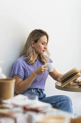 Frau liest ein Buch, während sie in einem Café Kaffee trinkt - PNAF01987