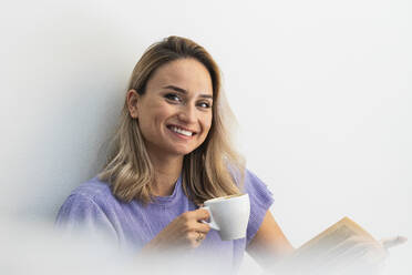 Beautiful woman with book smiling while having coffee at cafe - PNAF01988