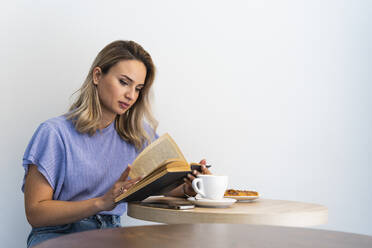 Young woman reading book at table in cafe - PNAF01990