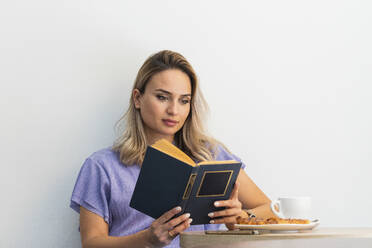 Beautiful woman reading book in front of wall at coffee shop - PNAF01991