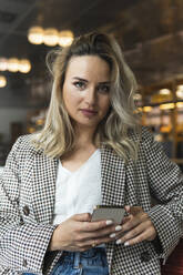 Schöne Geschäftsfrau hält Smartphone beim Sitzen im Café - PNAF02004