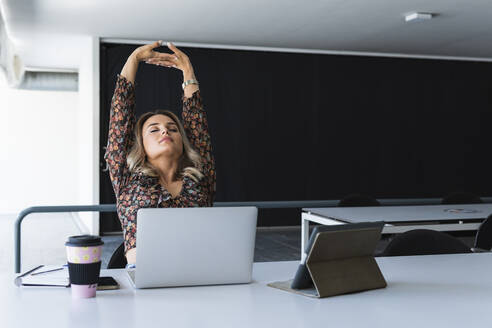 Tired businesswoman with arms raised relaxing at table in office - PNAF02013