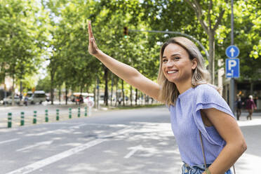 Smiling young woman hailing taxi on street - PNAF02019