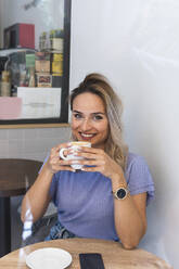 Lächelnde junge Frau trinkt Kaffee in einem Cafe - PNAF02021