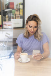 Frau, die ihr Smartphone benutzt, während sie in einem Geschäft Kaffee trinkt - PNAF02022