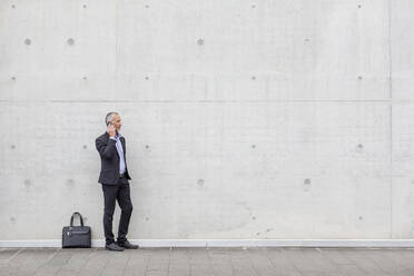 Geschäftsmann, der mit seinem Smartphone spricht, während er in der Nähe der Wand steht - EIF01304