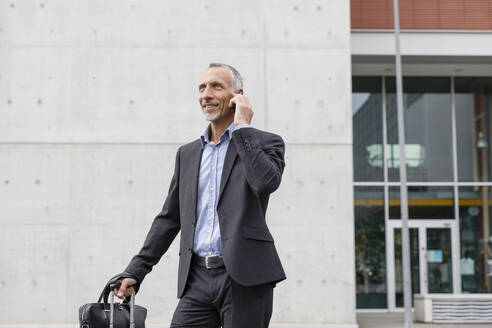 Businessman talking on smart phone while standing outside office building - EIF01310