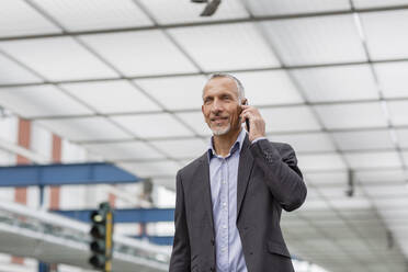 Businessman talking on smart phone at railroad station - EIF01316