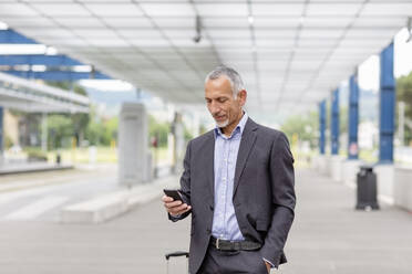 Männlicher Berufstätiger mit Smartphone am Bahnhof - EIF01319