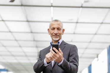 Smiling businessman using smart phone at railroad station - EIF01320