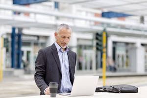 Geschäftsmann arbeitet am Laptop im Bahnhof - EIF01323