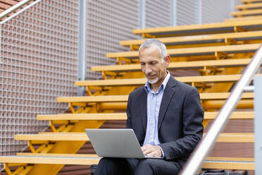 Businessman working on laptop while sitting on staircase - EIF01332