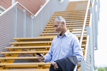 Businessman using smart phone while leaning on railing near steps - EIF01338