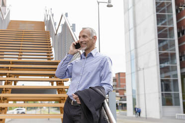 Businessman talking on smart phone while leaning on railing at steps - EIF01340