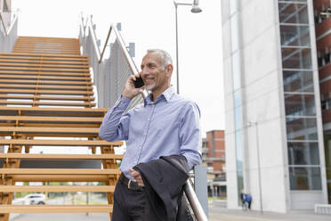 Geschäftsmann spricht mit seinem Smartphone, während er sich auf das Geländer einer Treppe stützt - EIF01340