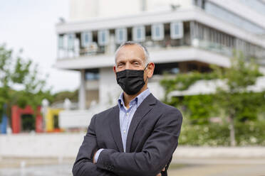 Businessman with protective face mask near building in city during COVID-19 - EIF01350