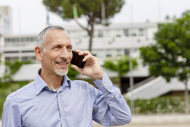 Geschäftsmann, der in der Nähe von Gebäuden mit einem Mobiltelefon spricht - EIF01358